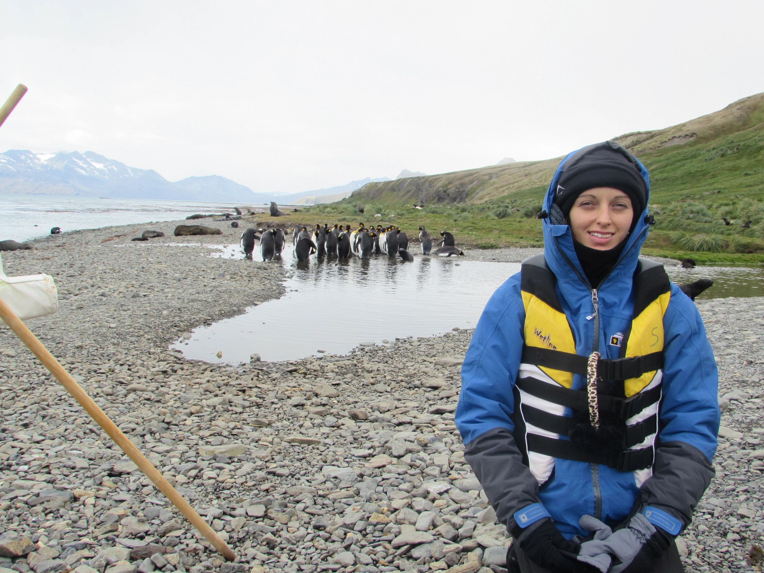 Deborah Langford in cold weather gear on an Antarctic beach with penguins